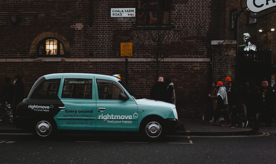 A classic London taxi parked on Chalk Farm Road with pedestrians passing by