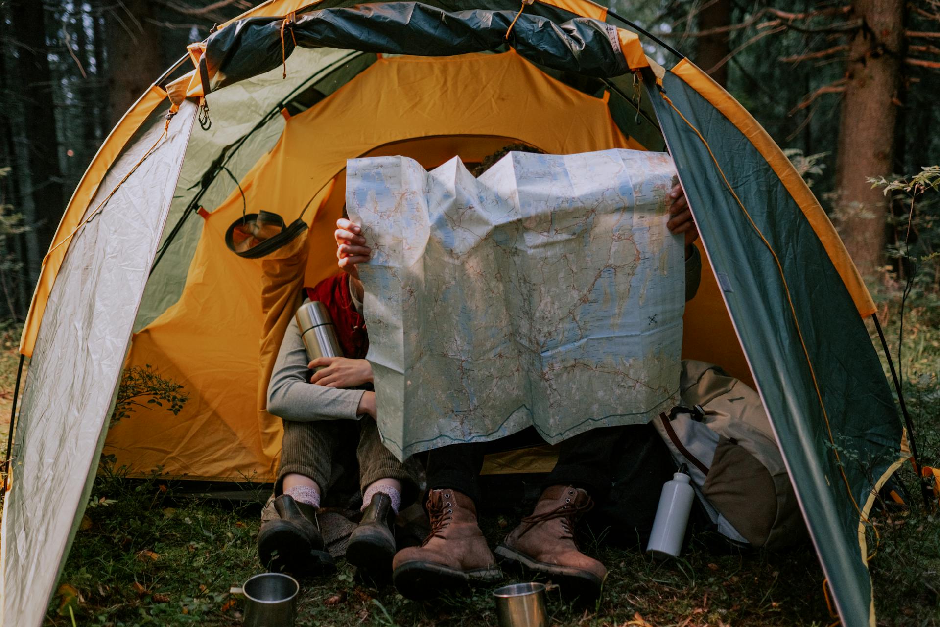 Two people enjoy a camping trip, examining a map inside a tent surrounded by nature.