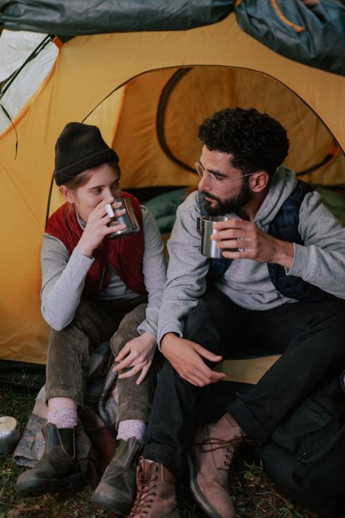 Free A couple sitting outside a tent, enjoying drinks in stainless steel cups. Stock Photo
