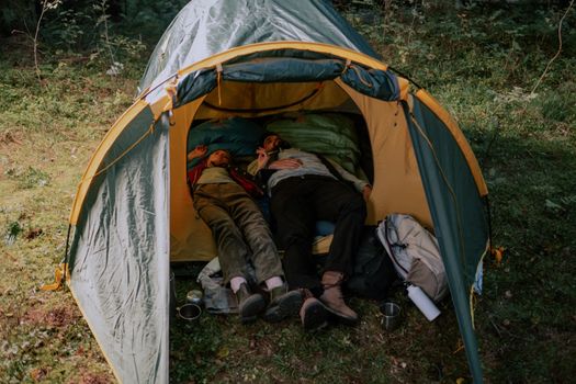 一对男女躺在郁郁葱葱的森林中的帐篷里，享受着宁静的露营时光