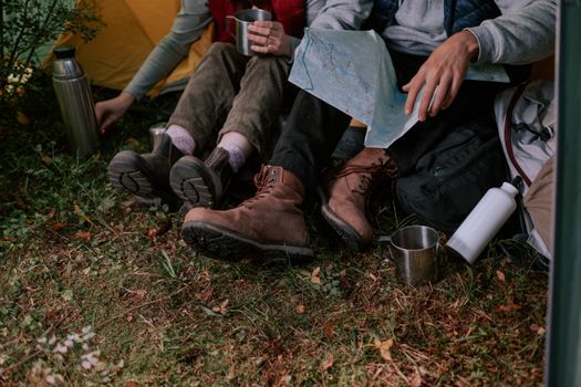 两个人在户外露营，穿着靴子，拿着地图，喝着饮料，享受放松时光