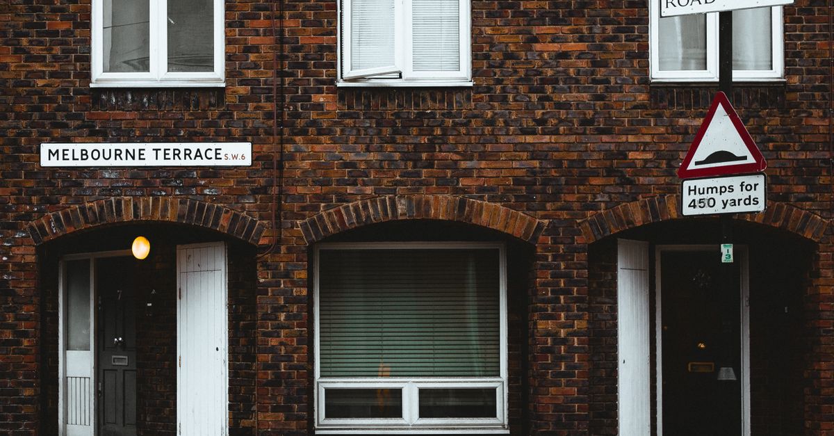 Facade of old brick residential building with plastic windows and jalousie near road with sign