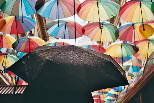 A black umbrella against a backdrop of colorful umbrellas strung above a city street.