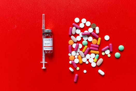 COVID-19 vaccine vial and colorful pills on a vibrant red surface.