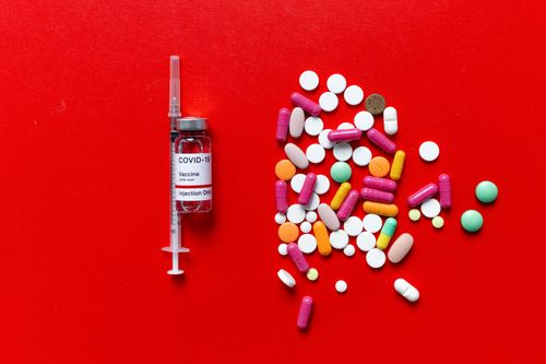 Free COVID-19 vaccine vial and colorful pills on a vibrant red surface. Stock Photo