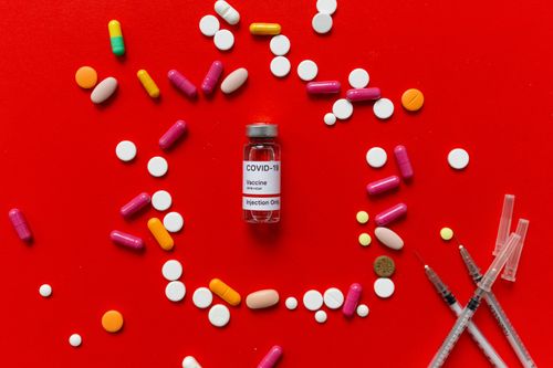 Free Colorful tablets and COVID-19 vaccine vial on a red background with syringes, symbolizing healthcare. Stock Photo