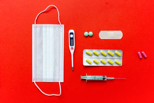 Free Flat lay of healthcare essentials including mask, thermometer, syringe, pills on red backdrop. Stock Photo