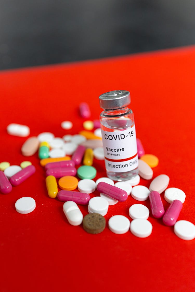 A Vial Of Vaccine And Pills On A Red Surface 