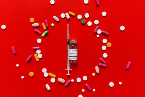 Free Vaccine vial and syringe surrounded by colorful pills on vivid red surface. Stock Photo