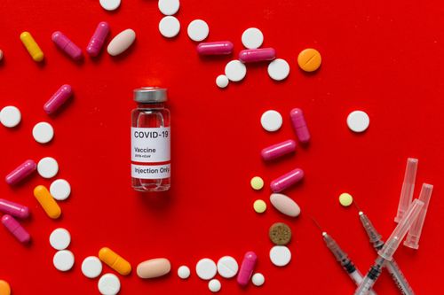 Free COVID-19 vaccine vial with various pills and syringes on a red background, symbolizing medicine and science. Stock Photo