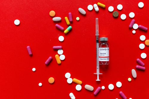 Free Close-up of COVID-19 vaccine vial with syringe and various pills on a red surface. Stock Photo