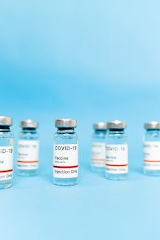 Multiple vials of COVID-19 vaccine arranged on a blue background.