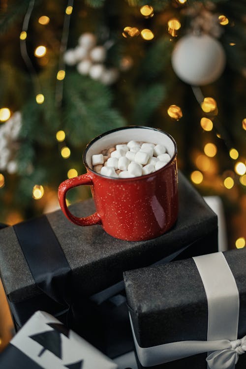 Free Hot Chocolate with Marshmellows Standing in front of a Christmas Tree on Boxes with Presents Stock Photo
