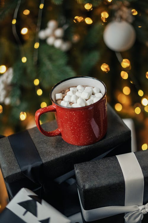 Hot Chocolate with Marshmellows Standing in front of a Christmas Tree on Boxes with Presents