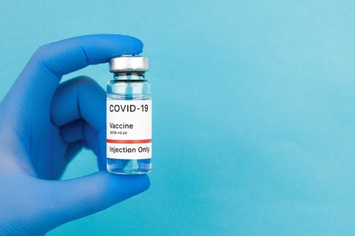 Free Close-up of a COVID-19 vaccine vial held by a hand in blue gloves against a blue background. Stock Photo