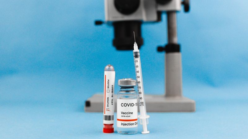 COVID-19 vaccine vial, syringe, test tube, and microscope on blue background, symbolizing research and healthcare.