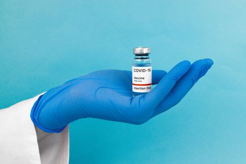 Free A COVID-19 vaccine vial held in a gloved hand on a blue background, symbolizing health care and protection. Stock Photo