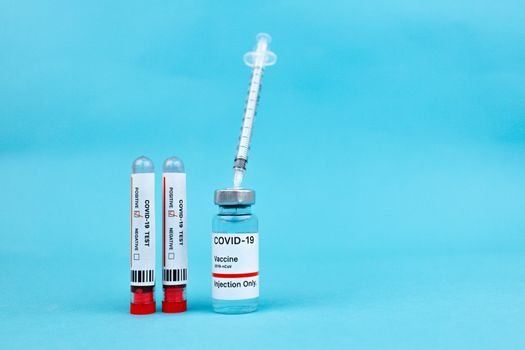 在蓝色表面上标记为新型冠状病毒肺炎的疫苗小瓶和血液试管，代表了医疗保健的进步