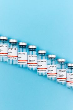 蓝色背景上，新型冠状病毒肺炎疫苗小瓶对齐排列，体现医疗保健概念