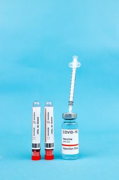注射器、新型冠状病毒肺炎疫苗小瓶和蓝色表面上的试管，代表着预防接种和预防