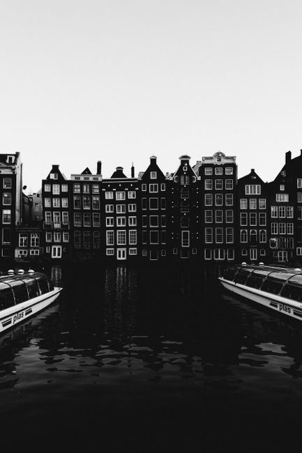 Black and white of water canal with boats flowing near aged residential buildings
