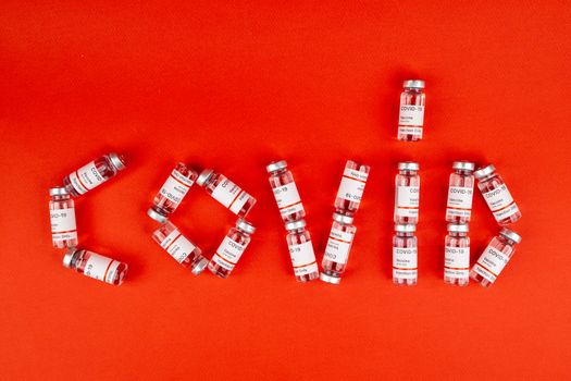 COVID-19 vaccine vials arranged to spell 'COVID' on a red surface.