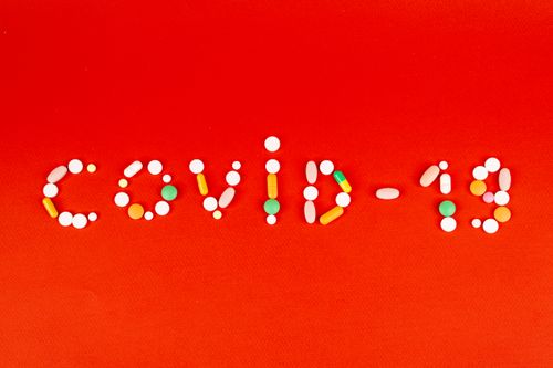 Free Pills arranged to spell COVID-19 on a vibrant red background, symbolizing medical response. Stock Photo