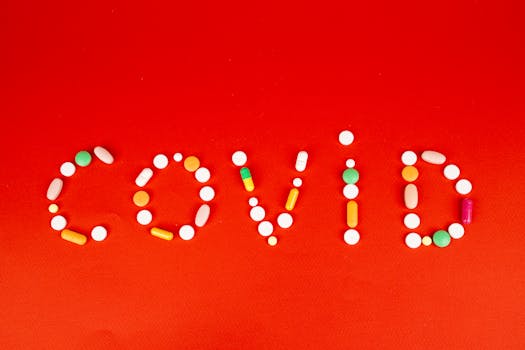 Colorful pills form the word 'COVID' on a bright red background, symbolizing healthcare.