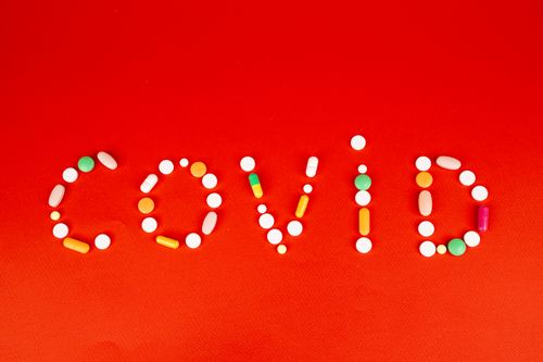 Free Colorful pills form the word 'COVID' on a bright red background, symbolizing healthcare. Stock Photo