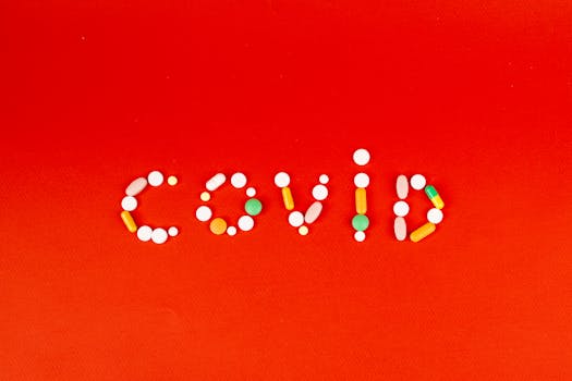 COVID spelled using assorted pills on a vibrant red background, symbolizing pandemic and medication.