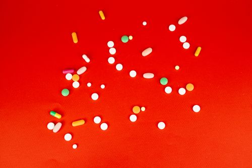 Free A colorful assortment of pills and capsules scattered on a bright red surface. Healthcare and medication concept. Stock Photo