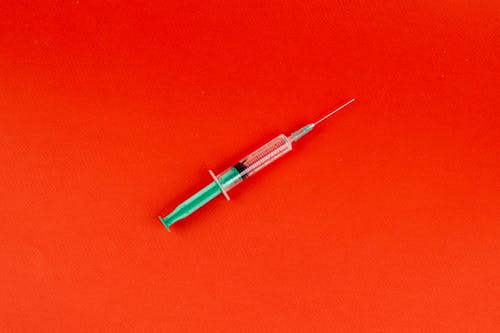 Free Syringe With Needle on a Red Surface Stock Photo