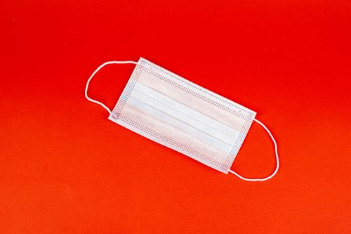 Free White disposable face mask on a bright red surface, emphasizing protection and safety. Stock Photo