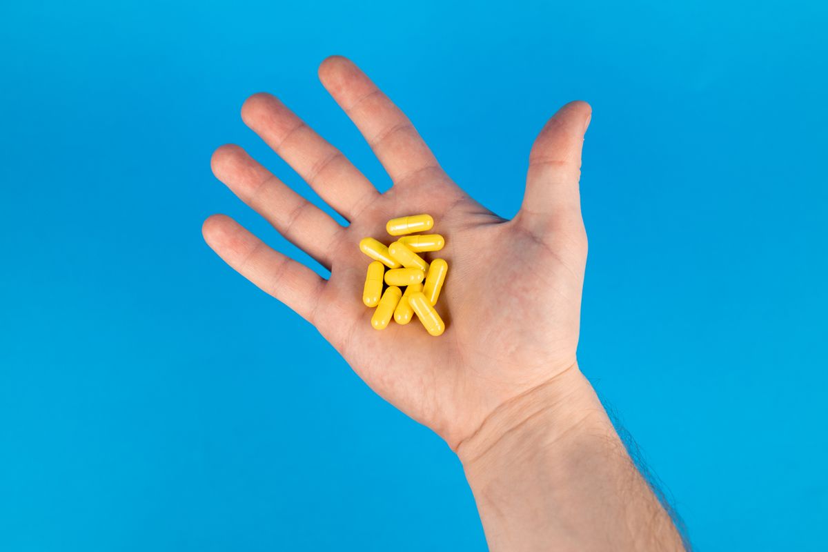 Mao segurando capsulas amarelas de suplemento contra fundo azul