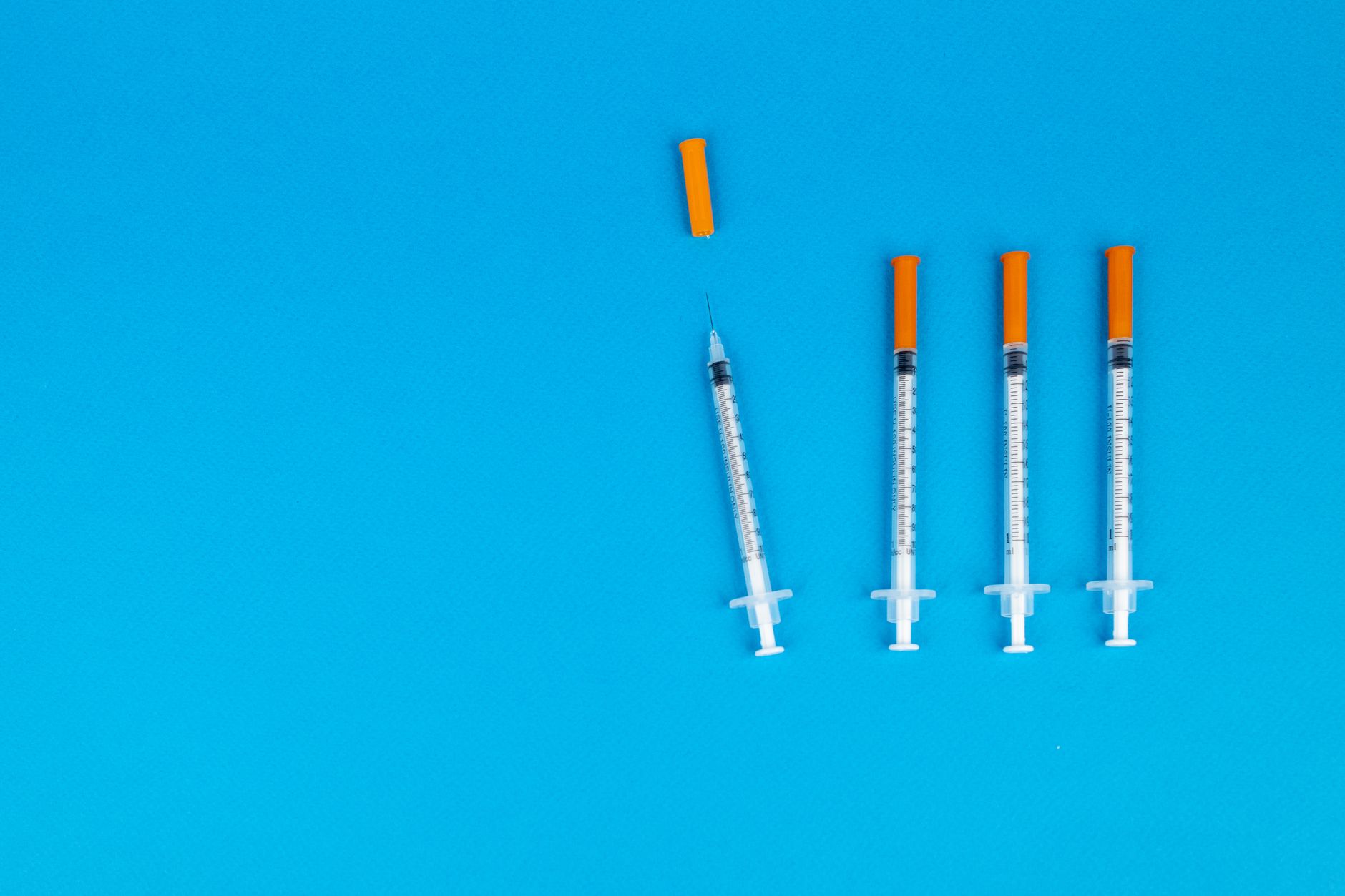 Four medical syringes with orange caps on a vivid blue background, ideal for healthcare or vaccination themes.