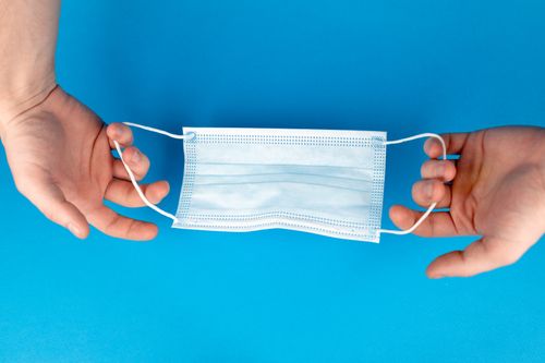 Free Close-up of hands holding a surgical mask on a vibrant blue background. Stock Photo