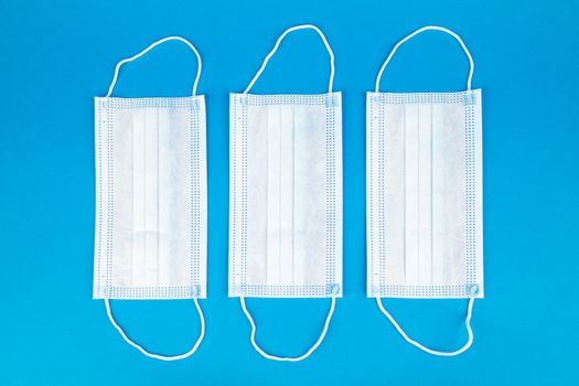 Three white medical masks arranged on a vibrant blue background, flat lay view.
