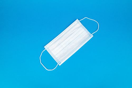 Free Disposable white face mask on vibrant blue backdrop, symbolizing health protection. Stock Photo