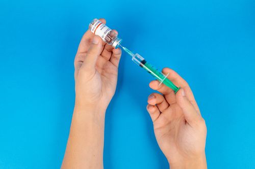 Free Hands holding a syringe and COVID-19 vaccine vial on a blue background. Stock Photo