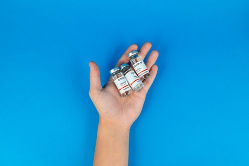 Free Close-up of a hand holding COVID-19 vaccine vials on a blue background, representing pandemic measures. Stock Photo