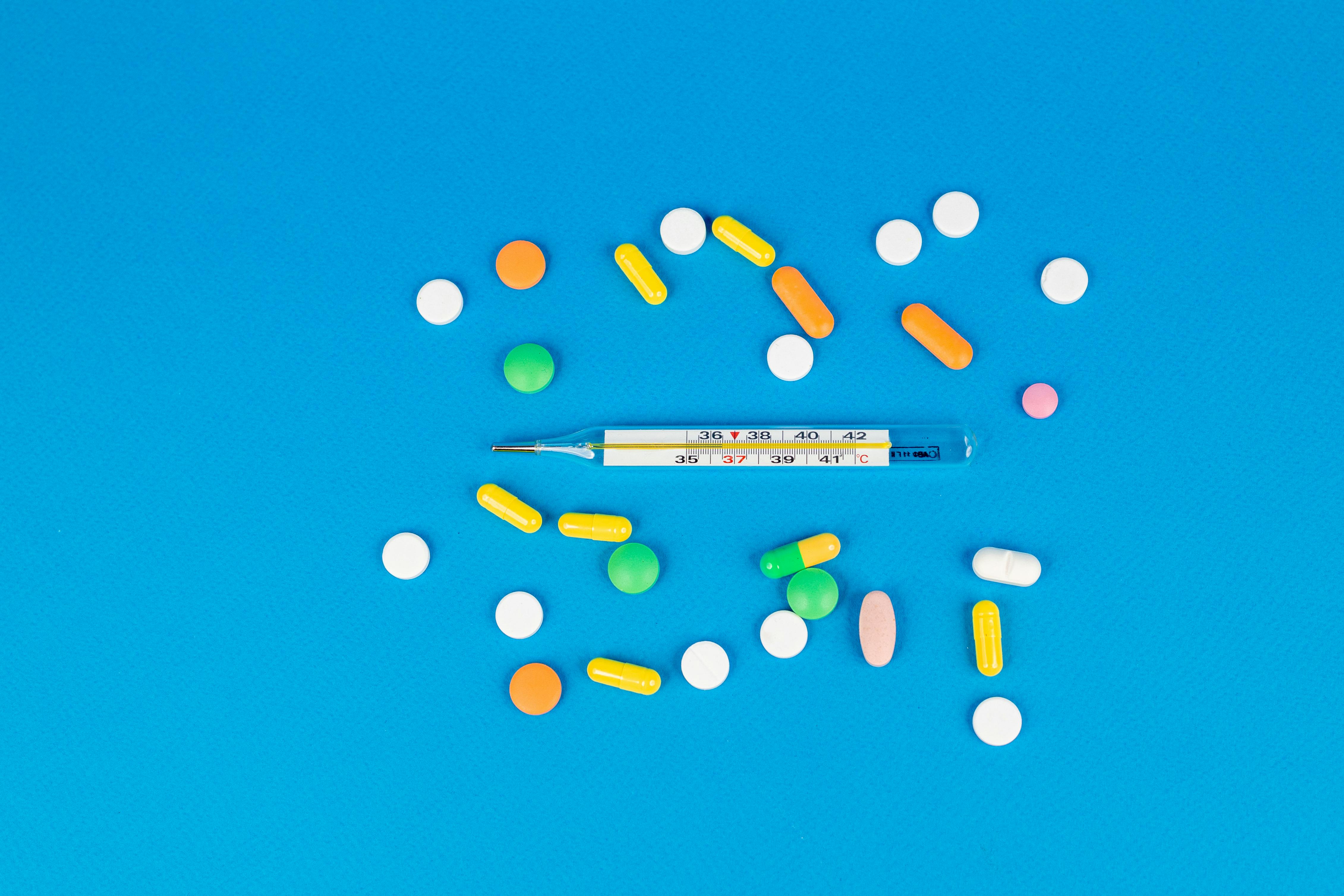 Vibrant pills and a thermometer arranged on a blue backdrop. Perfect for health and medicine themes.