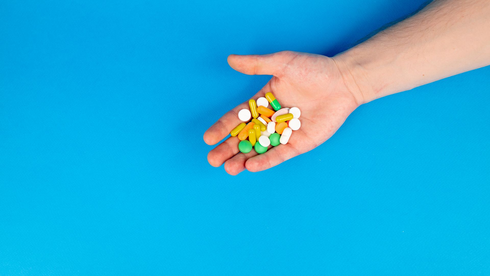 Modafinil vs Adderall: Unlocking the Secrets of Cognitive Enhancement A hand holding a variety of colorful pills against a blue background with ample copy space — modafinil vs adderall