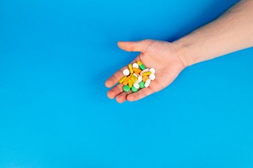 Free A hand holding a variety of colorful pills against a blue background with ample copy space. Stock Photo