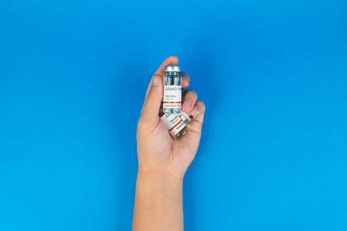 Free Close-up of a hand holding COVID-19 vaccine vials against a bright blue background, symbolizing vaccination efforts. Stock Photo