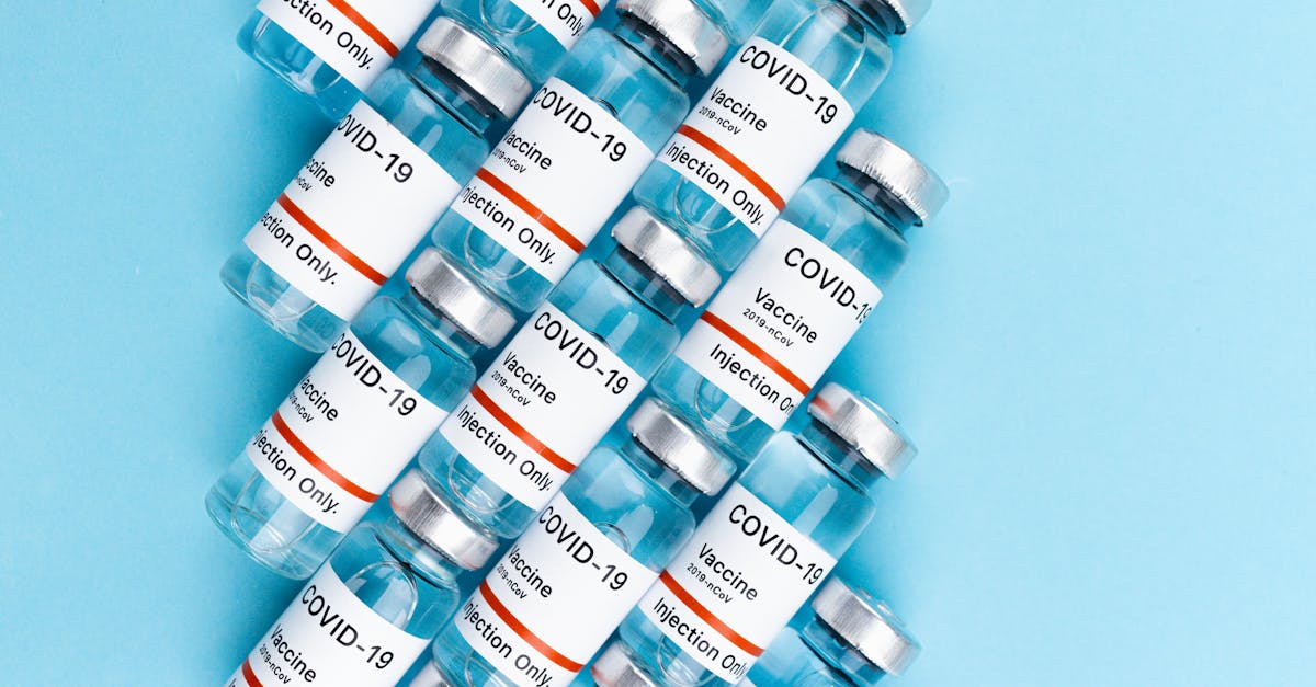 Photo by Maksim Goncharenok Top view of COVID-19 vaccine vials arranged on a blue surface, highlighting vaccination and pandemic themes.