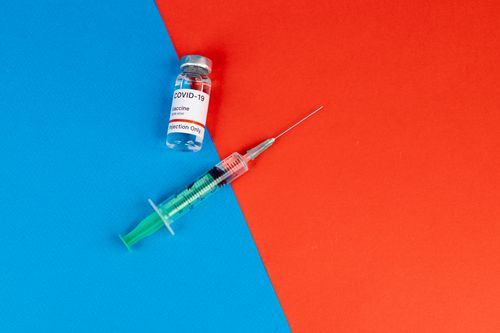 Free Close-up of a Covid-19 vaccine vial and syringe on a blue and red background, symbolizing pandemic. Stock Photo