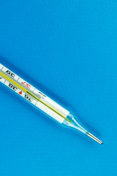 Close-up of a mercury thermometer on a blue background captured in a studio setting.