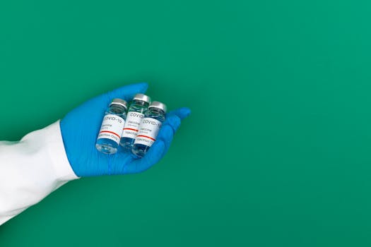 A gloved hand holding COVID-19 vaccine vials against a green backdrop offers medical and health protection imagery.