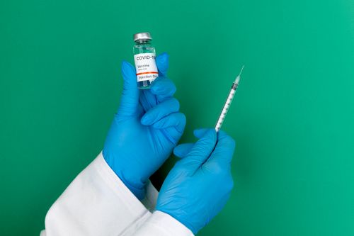 Free Medical professional holding a COVID-19 vaccine vial and syringe in a studio setting with green background. Stock Photo