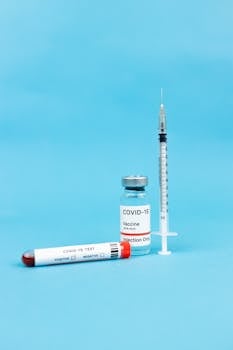 COVID-19 vaccine vial, syringe, and test tube on a blue background, symbolizing pandemic healthcare.